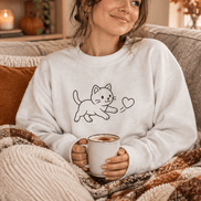 Cat Heart Crewneck Sweatshirt worn by a young woman sitting on a couch with a cocoa