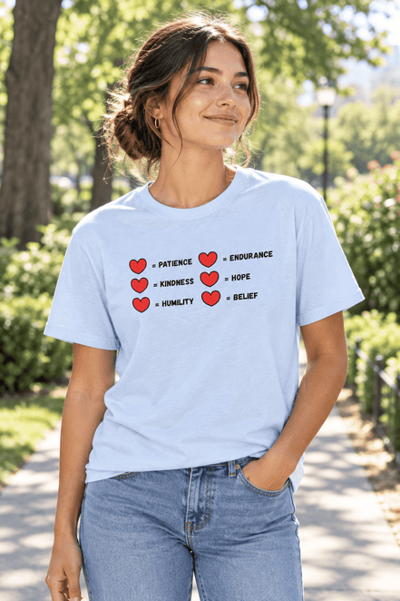 A  tee worn by young woman in jeans outside tee has a two rows of hearts with equal signs. in a row next to the = signs are the words "patience, kindness, humility, endurance, hope, belief"