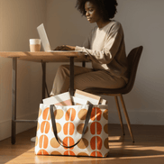 A woman sits at a desk with a large bag with a geometric pattern next to her.
